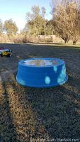 Blue round stock tank set on grass outdoors, showing full outer view and size relative to surroundings.