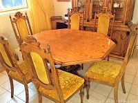 Front view of five of the six wooden dining chairs arranged around a wooden dining table under a window with yellow curtains