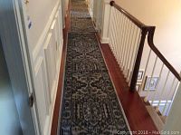 Long hallway view showing the 12 ft runner in silver and black with ornate traditional design next to white paneled walls and wood flooring.