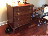 Dresser front view showing four drawers and brass hardware on wooden floor near wall and chair