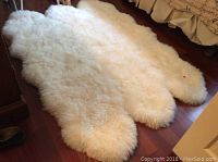 Full view of the white sheepskin area rug laid out on hardwood floor showing its size and fluffy texture.