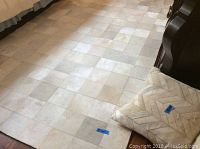 Full view of rectangular area rug on floor near furniture and bedding; shows square patches of cowhide in cream and beige tones, slight wear visible.