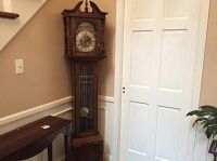 Full view of oak-finish wooden grandfather clock case with arched bonnet top and glass door
