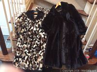 Two full length fur coats displayed hanging over a wooden banister