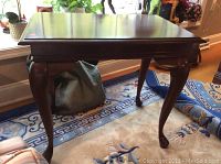 Full view of the dark wood side table with curved legs on a patterned rug, showing overall shape and style.