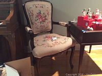 Frontal view of one needlepoint upholstered armchair showing carved wood frame and floral needlepoint seat and back.