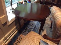 Photo showing the round tabletop in the extended position next to a striped upholstered chair and patterned rug.
