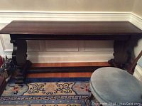 Full view of dark wood antique console table against wall on patterned rug