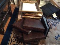 Stack of assorted picture frames mostly wooden and gold-toned with some prints inside, stacked on a rug.