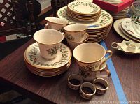 Photo showing holiday-themed Lenox china with holly and berries pattern including teacups, saucers, and plates stacked neatly on a table.