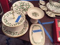 Overview of four Lenox serving pieces with holly pattern on table, including two-tier dish, cake plate, footed candy dish, and rectangular plate with blue tape showing dimensions