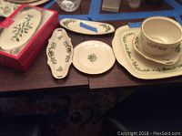 Photo of Lenox Holiday Archive cream porcelain serving dishes with holly and berry pattern, some pieces have blue tape sizing and notes, show tray, olive dishes, candy dish, and cup with saucer.