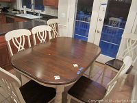 Six wooden Primo dining chairs arranged around a dark wood dining table with cream turned legs, shown in kitchen setting.
