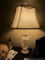 Image showing the lamp illuminated with the fabric lampshade on, highlighting the crystal base's cut pattern under light.