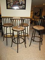 Four metal bar stools with upholstered seats and vertical bar backrests arranged on carpeted floor in basement area.