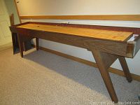 Long wooden shuffleboard table with laminate playfield, four legs and metal corner protectors