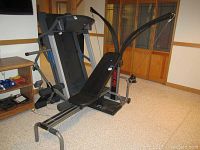 Photo showing the full Bowflex Power Pro exercise machine with padded bench, resistance rods, and cable arms set up in a basement room.