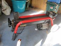 Side view of the Homelite wood splitter showing the red frame, motor, and splitting wedge mounted low to the ground.