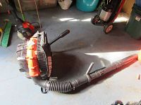 Front view of backpack blower assembly on floor, showing motor housing, flexible hose and blower tube.