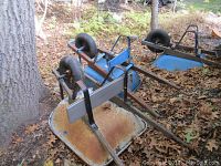 Three metal wheelbarrows with wooden handles, placed upside down on leafy ground outdoors, showing rust and wear on metal trays and frames.