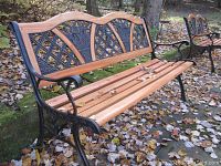 Front-side angle of garden bench showing wood slats and decorative metal backrest with floral motifs.