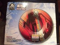 Photo of the snow tube in its original packaging box highlighting brand, product name, and key features such as heavy-duty handles and vinyl construction.