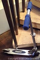Front side view of the Razor scooter showing the deck, part of the adjustable handlebar with blue foam grips, and rear fender brake.