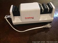 White Chef's Choice Diamond Hone 110 electric knife sharpener shown on brown surface, with power cord extended and plug visible.