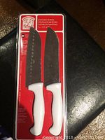 Two Santoku knives in sealed blister packaging with white handles and visible red backing card.