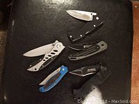 Lot of 5 assorted pocket knives displayed on a black surface, showing overall lot content and variety.