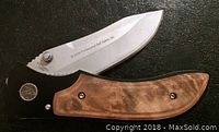 Photo of folding knife showing wood handle and metal blade with Professional Bull Riders inscription.