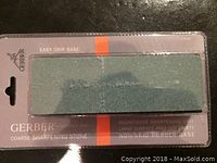 Photo of Gerber coarse sharpening stone in unopened packaging showing green abrasive stone on black rubber base with product branding and features visible