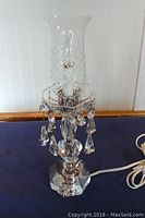Photo of the full vintage crystal hurricane lamp showing cut glass hurricane shade, hanging crystal prisms, faceted crystal lamp base, and power cord on dark fabric background.