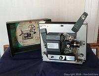 Full view of the Bell and Howell movie projector and its open carrying case with instruction guide.