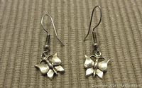Pair of sterling silver butterfly-shaped dangle earrings shown front-side up on a fabric surface, displaying their design details and hook closures.