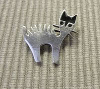 Front view of sterling silver cat brooch showing black enamel on the face and whimsical design with whiskers and spikes along the back.