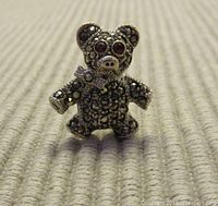 Front view of small bear brooch showing marcasite stones, red glass eyes, and textured sterling silver.