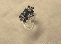 Front view showing two flower clusters with clear center stones and surrounding blue stones on sterling silver band.