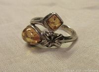 Lightweight sterling silver ring with two amber stones, diamond and teardrop shaped, floral motif and open band design.