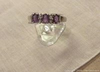 Front view of the sterling silver amethyst ring with three oval stones and clear gemstone accents on fabric surface.