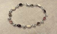 Full view of linked sterling silver bracelet with multiple oval bezel set amber stones in various colors on a light gray fabric background.