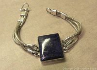 Sterling silver lapis lazuli bracelet laid flat, showing stone and triple snake chains with hook closure.