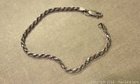 Full view of the twisted rope silver chain bracelet laid flat on fabric background, showing lobster clasp and chain end.