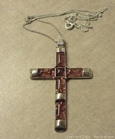 Sterling silver cross pendant with inset Baltic amber stones displayed flat showing front side of cross with amber stones set in four arms and center.