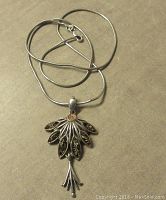 Full view of the sterling silver pendant and chain laid flat showing the pendant design and chain coiled