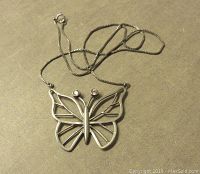 Photo of open work sterling silver butterfly pendant with two clear cubic zirconia stones on 15 inch silver chain, shown flat on beige surface.