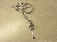Photo showing the front of the vintage sterling silver key pendant on the chain. The key features four tiny heart shapes and a red stone near the top below the bail. The chain is visible loosely coiled.