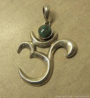 Front view of the sterling silver Celtic triskele pendant with bezel set green stone on a neutral background.
