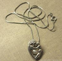 Overall view of the sterling silver mother and child pendant on the box chain, laid flat to show chain design and pendant scale.