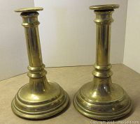 Front view of two brass candlesticks showing cylindrical stem and stepped round base.